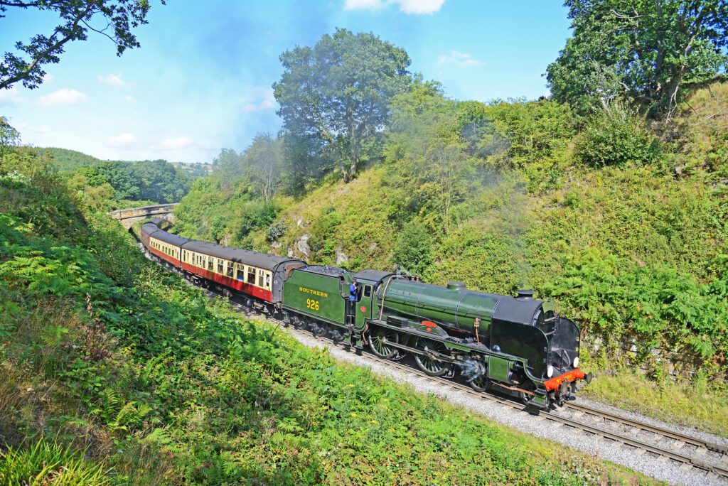 A green steam locomotive on a railway through a green hills