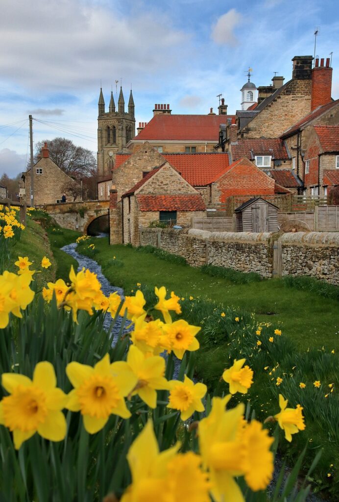 a stream runs alongside red-tiled cottages and an old church, with daffodils in the foreground