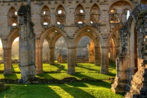 Stone arches and walls of a ruined monastery, casting shadows over sunlit grass