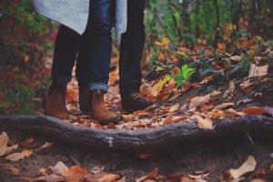 A woman and man walk through a woodland path covered in leaves. You can only see their trousers and boots